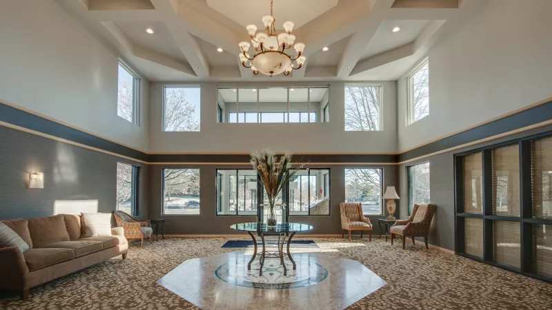 Elegant, spacious lobby with high ceilings, a grand chandelier, large windows, a sofa, chairs, and a central glass table.