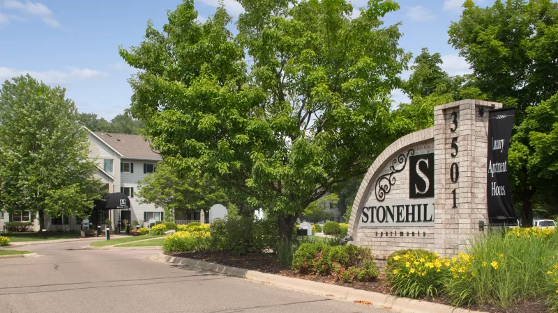 Stonehill Apartment Homes entrance sign with address 3501, surrounded by green trees and yellow flowers.