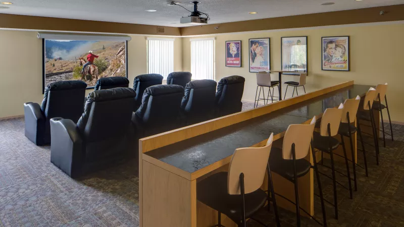 Home theater with a large screen displaying a western, black reclining seats, and a back counter with stools.