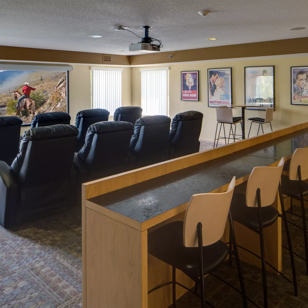 Home theater with a large screen displaying a western, black reclining seats, and a back counter with stools.