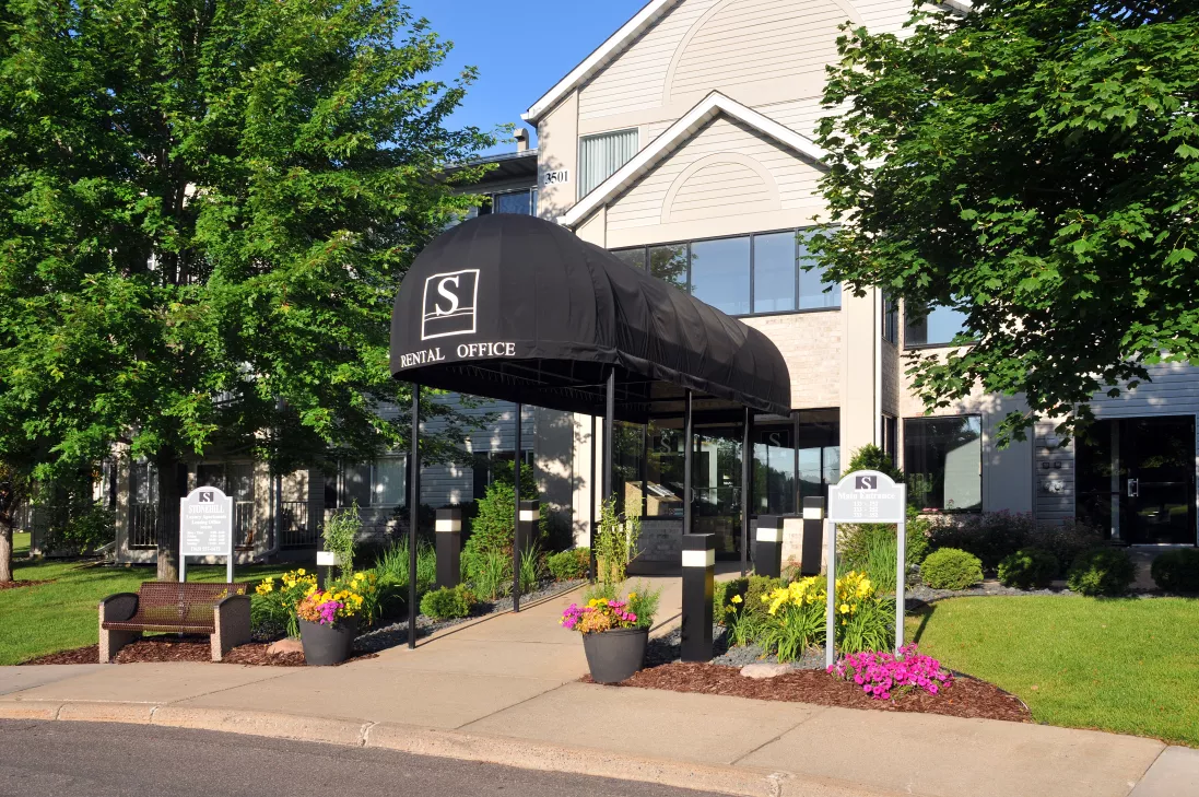 Building entrance with black "South Shore" awning, surrounded by vibrant green trees and colorful flowers in pots.